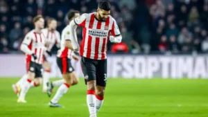 PSV Eindhoven player, Sebari, walks with a disappointed expression after a missed opportunity, with teammates in the background during a match.
