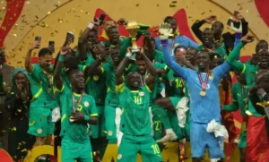 L'équipe de football du Sénégal célèbre sa victoire à la Coupe d'Afrique des Nations, brandissant le trophée, entourée de confettis et de coéquipiers en tenue verte.
