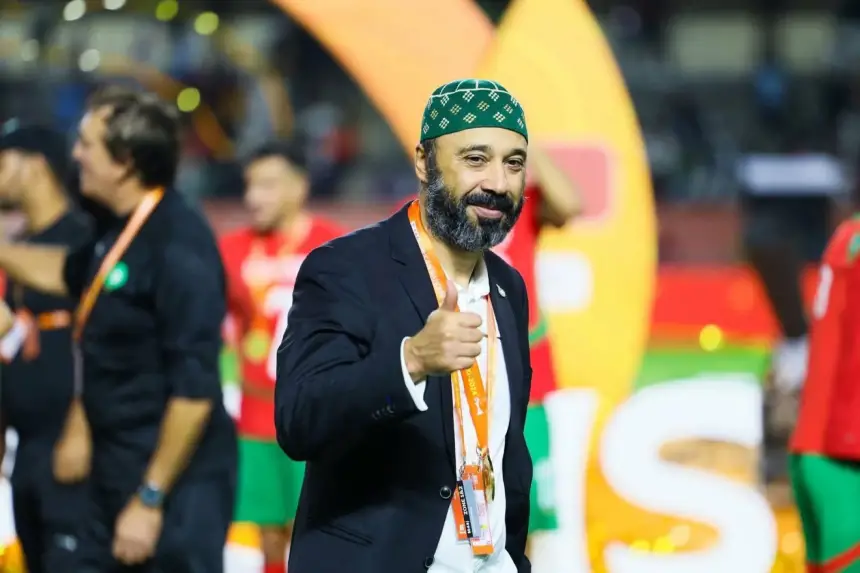 Moroccan football official giving a thumbs-up, wearing a green hat, celebrating a victory in a vibrant stadium filled with team colours.