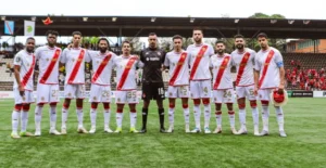 Le onze de départ du Wydad Casablanca pose pour une photo d'équipe dans leur tenue rouge et blanche, avec les joueurs et le gardien de but sur un terrain vert.