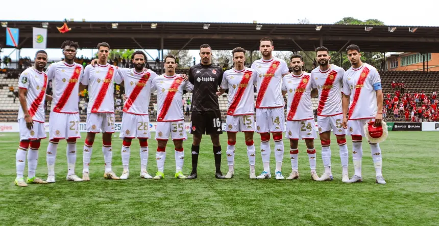 Le onze de départ du Wydad Casablanca pose pour une photo d'équipe dans leur tenue rouge et blanche, avec les joueurs et le gardien de but sur un terrain vert.