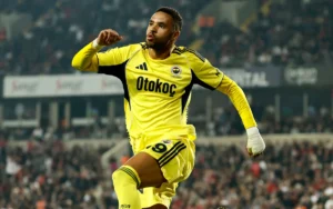 Youssef En-Nesyri celebrates after scoring for Al Ittihad in a vibrant match atmosphere, clad in a bright yellow kit.