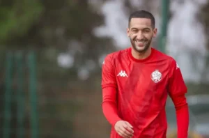 Hakim Ziyech smiles during training in a red Wydad Casablanca jersey, showcasing his cheerful spirit before a crucial match.