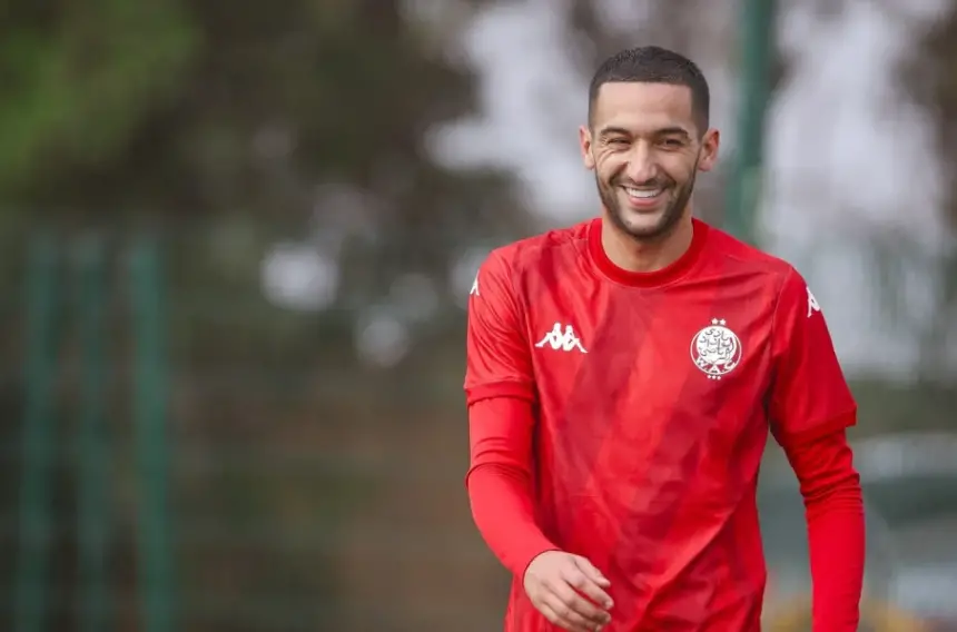 Hakim Ziyech smiles during training in a red Wydad Casablanca jersey, showcasing his cheerful spirit before a crucial match.