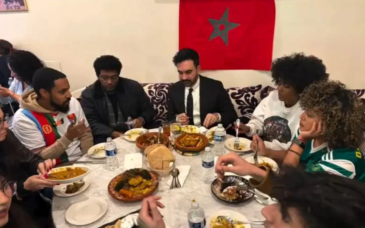 Group enjoying Moroccan cuisine at a table laden with dishes, with a Moroccan flag prominently displayed in the background.
