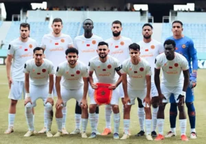 Al Nahda Berkan team posing for a team photo in white kits, showcasing their Moroccan pride with the national flag.