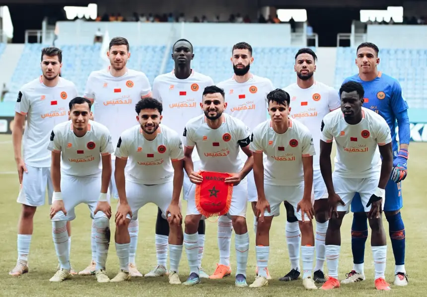 Al Nahda Berkan team posing for a team photo in white kits, showcasing their Moroccan pride with the national flag.